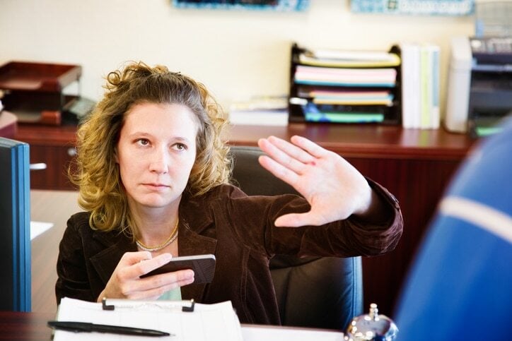 A somewhat lousy receptionist tells a visitor to wait until she finishes her video game level before asking for help.