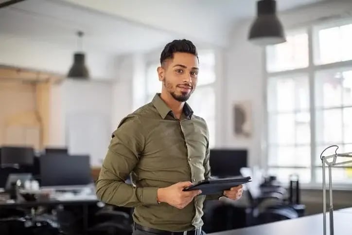 Portrait of young businessman standing in office with digital tablet in hand. Male professional looking at camera.